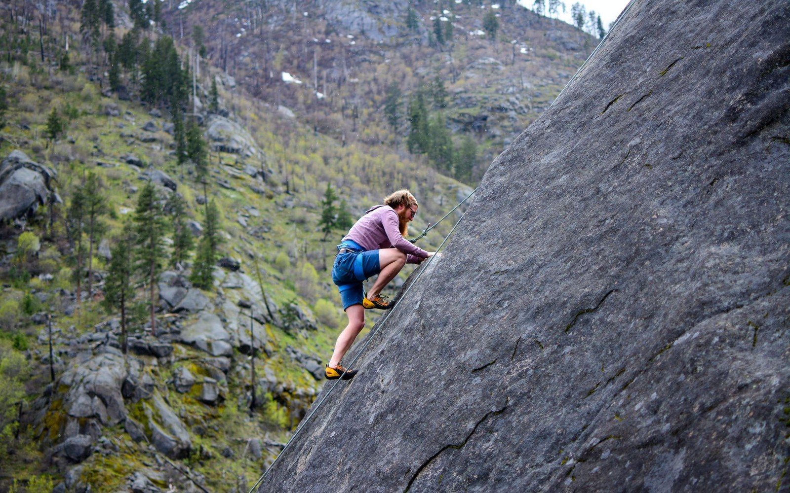 Climber scales a steep granite slab above a forested valley near Leavenworth