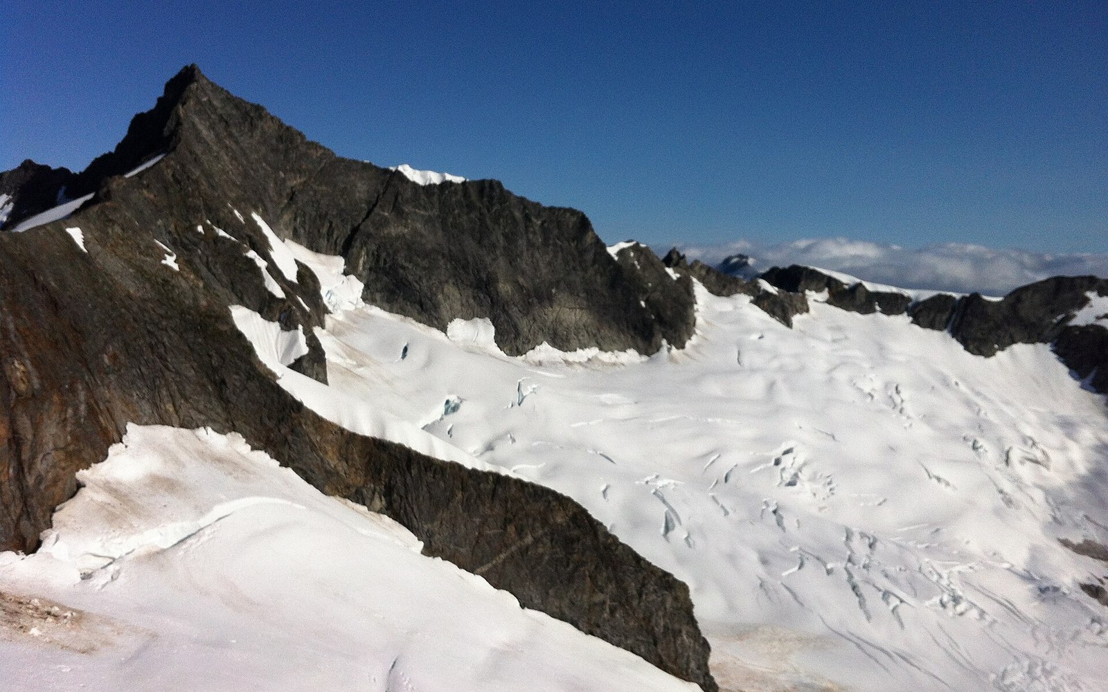 Snow-covered glacier and crevasses beneath a jagged rocky ridge under clear sky