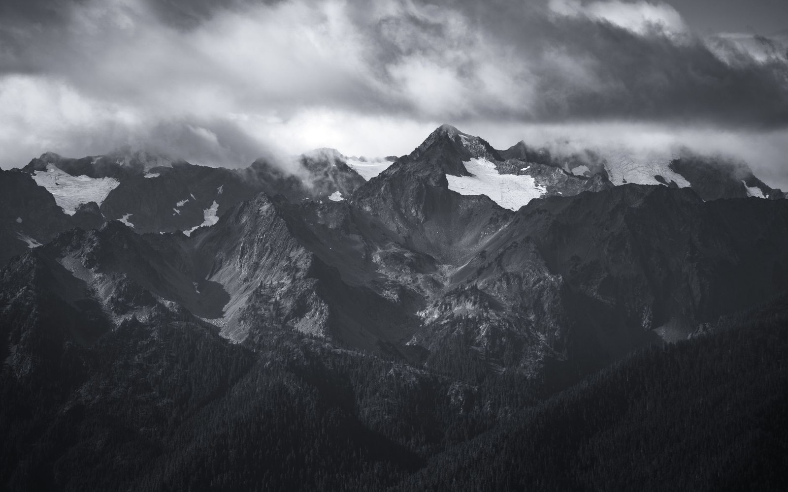 Snow-streaked mountain peaks rise beneath heavy storm clouds in black and white