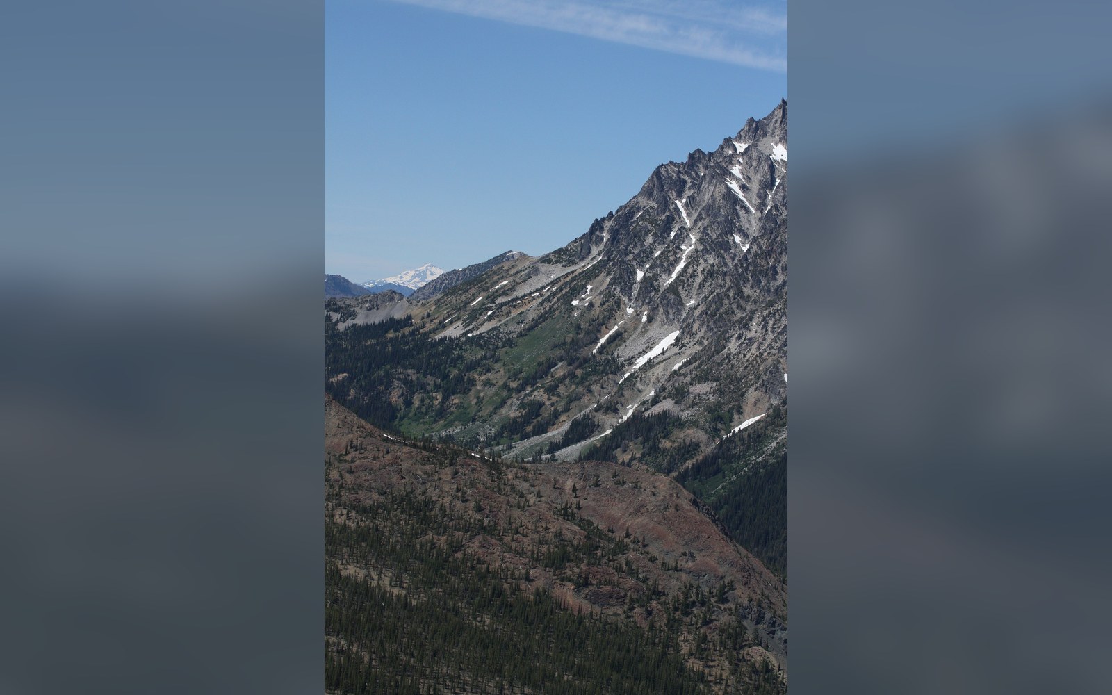 Snow-streaked mountain ridge rises above a forested valley under clear sky