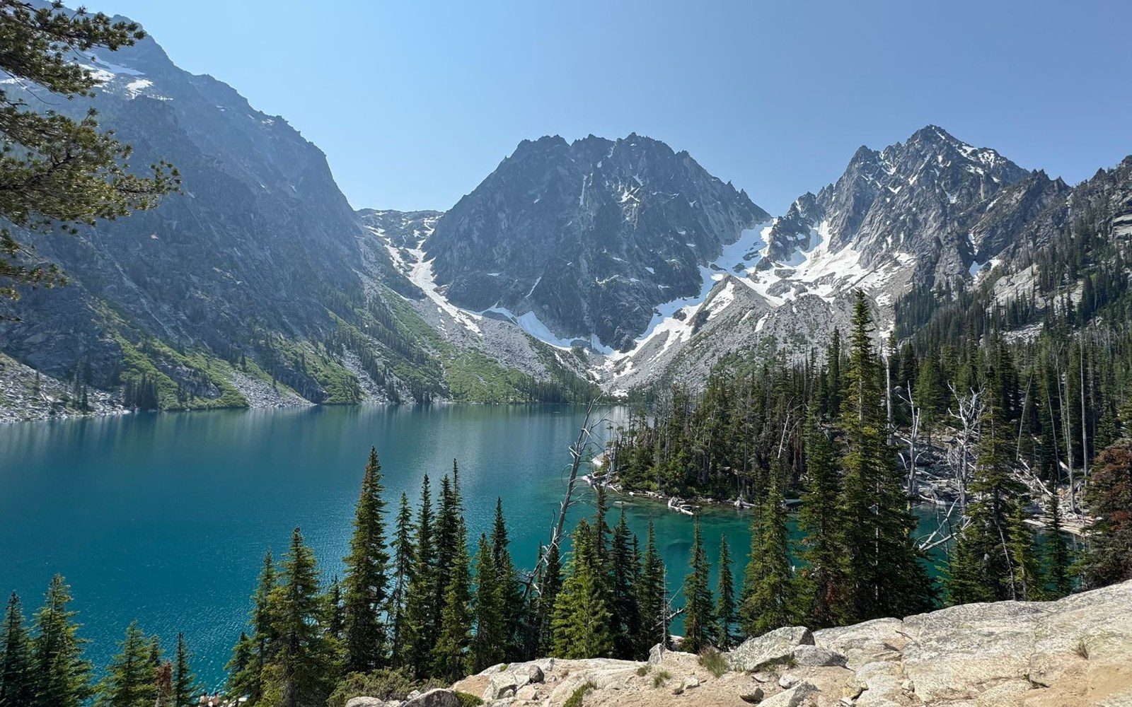 Turquoise alpine lake surrounded by jagged snow-capped peaks and evergreen trees